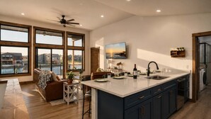 Una cocina moderna con una isla grande, piso de madera y vista al agua a través de amplios ventanales.