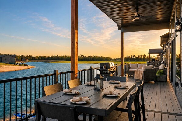 A covered outdoor dining area with a view of a body of water and a distant shoreline.