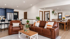 Una sala de estar moderna con un sofá de cuero marrón, una mesa de centro de madera y un comedor con mesa y sillas de madera.