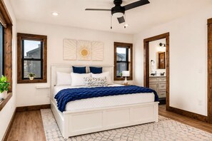 A bedroom with a bed, a ceiling fan, a window, a nightstand, and a bathroom visible through an open door.