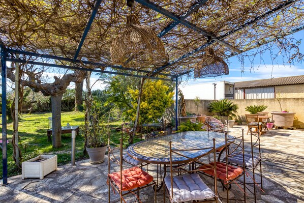 Eine überdachte Terrasse mit einem runden Tisch, Stühlen und einer hängenden Lampe.
