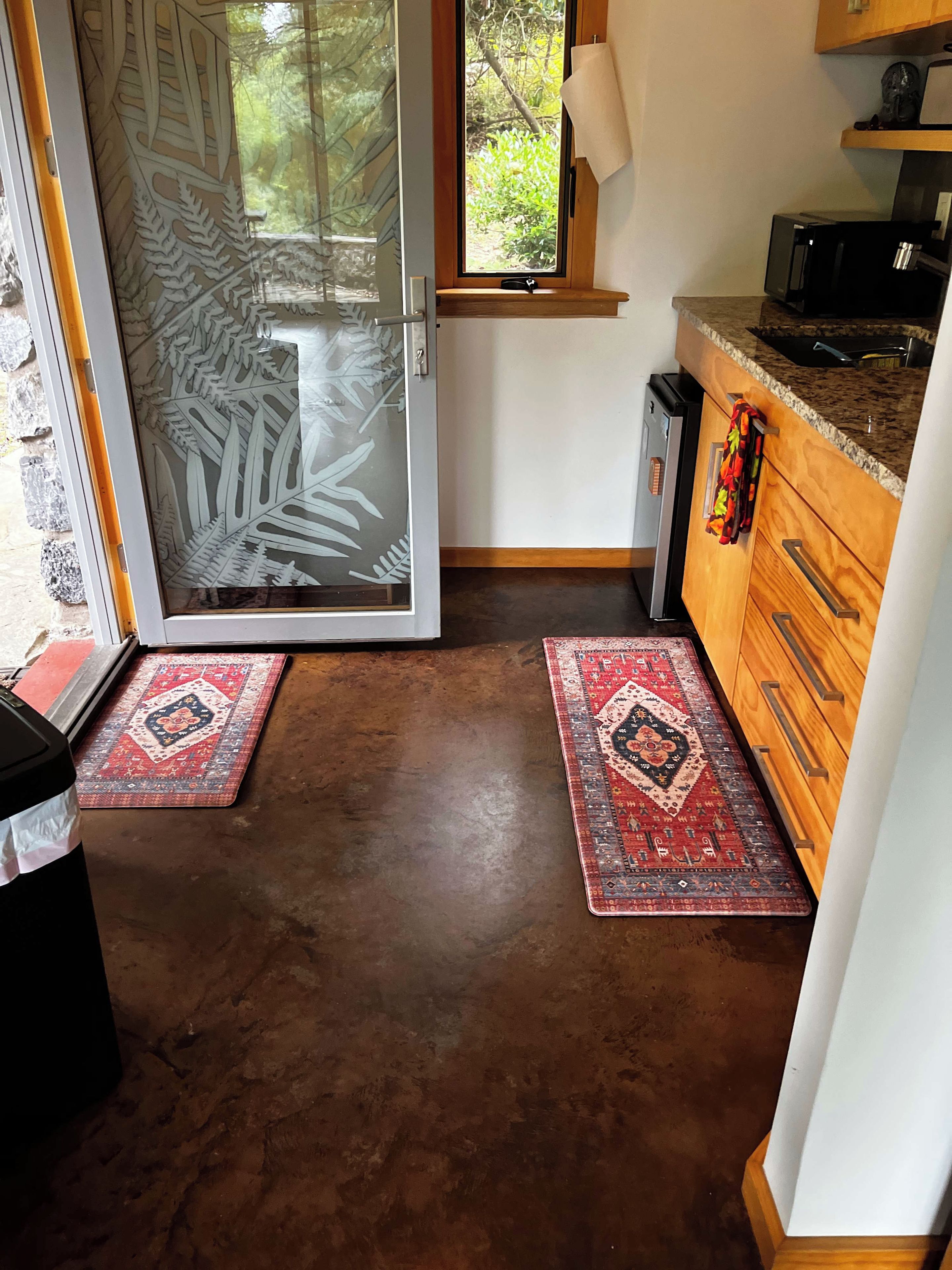 A kitchen with a sliding glass door leading to a garden, a microwave, and a wooden cabinet.