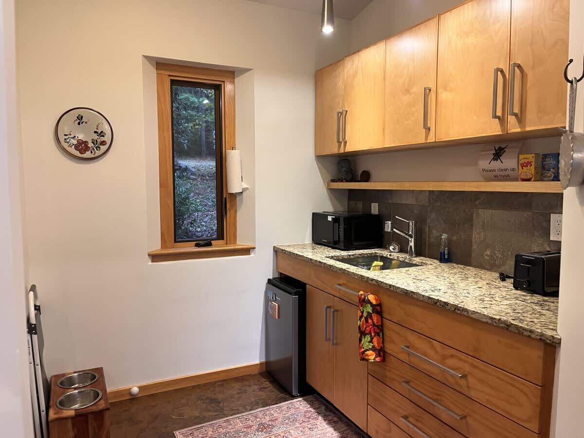 A compact kitchen with wooden cabinets, a granite countertop, a built-in microwave, and a small refrigerator.