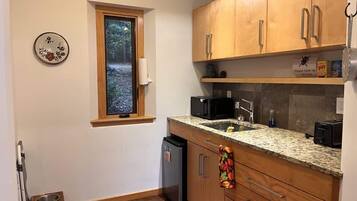 A compact kitchen with wooden cabinets, a granite countertop, a built-in microwave, and a small refrigerator.