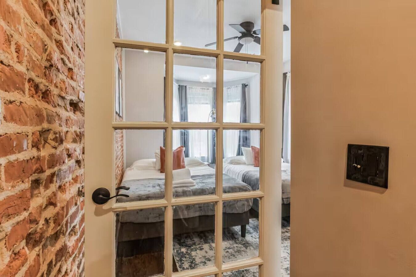 A room with a brick wall, a large window with multiple panes, and a ceiling fan.