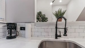 Een moderne keuken met witte metrotegels, een RVS-spoelbak, een zwarte koffiezetapparaat en een potplant.