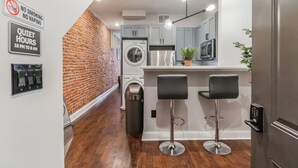 Een moderne keuken met een bakstenen muur, een wasmachine, een magnetron en twee barkrukken.