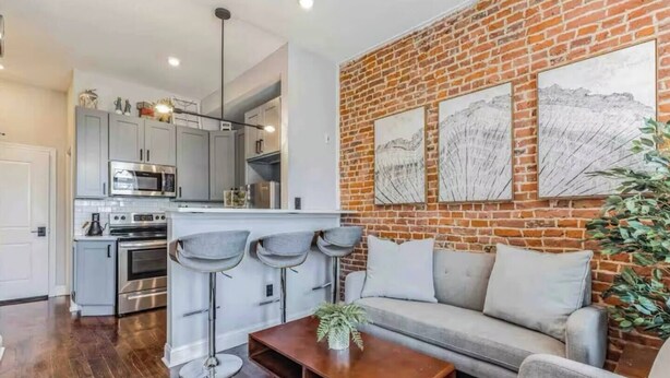A modern living room with a grey sofa, a wooden coffee table, and a kitchen in the background. - Studio w/Terrace | Street Parking | 10 min to DT (Philadelphia)
