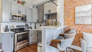 A modern kitchen with stainless steel appliances, white cabinetry, and a brick wall. - Studio w/Terrace | Street Parking | 10 min to DT (Philadelphia)