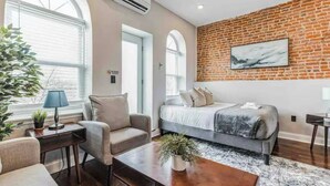 A modern room with a brick wall, a bed, a sofa, and a coffee table. - Studio w/Terrace | Street Parking | 10 min to DT (Philadelphia)