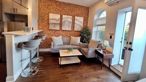 A modern living room with a brick wall, a sofa, a coffee table, and a bar area with stools. - Studio w/Terrace | Street Parking | 10 min to DT (Philadelphia)