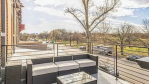 A balcony with wicker furniture, a glass table, and a view of a parking lot and trees. - Studio w/Terrace | Street Parking | 10 min to DT (Philadelphia)