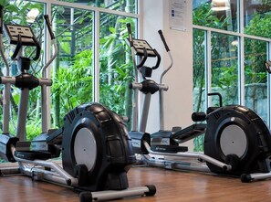 A row of stationary bikes in a room with large windows and a view of greenery outside.