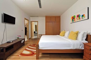 Een slaapkamer met een bed, een houten garderobe, een televisie en een schilderij aan de muur.