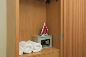 Een houten garderobe met een klein plankje waarop een witte handdoek en een rood-witte strijkijzer liggen.