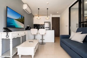 A modern living room with a TV, a coffee machine, and a kitchen area with a fridge. - Suite Calypso 1br| Palmyrah Surin 300m to beach (Choeng Thale)