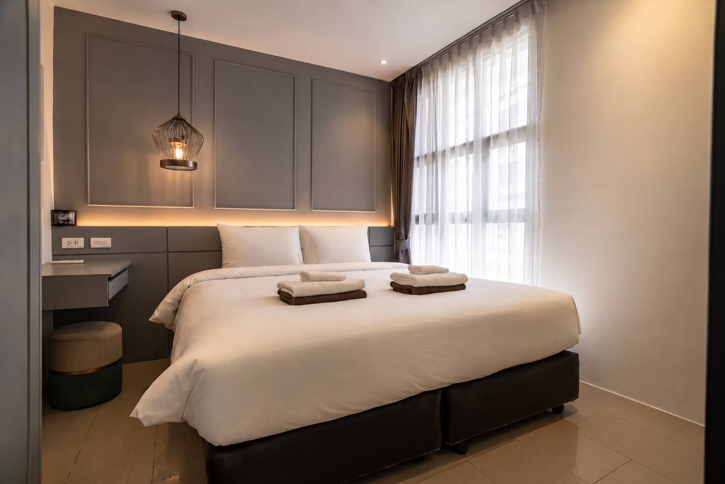 A modern hotel room with a large bed, bedside tables, a desk, and a pendant light.