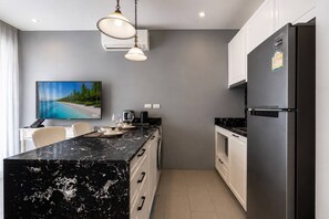 A modern kitchen with a marble countertop, stainless steel appliances, and a flat-screen TV mounted on the wall. - Suite Calypso 1br| Palmyrah Surin 300m to beach (Choeng Thale)