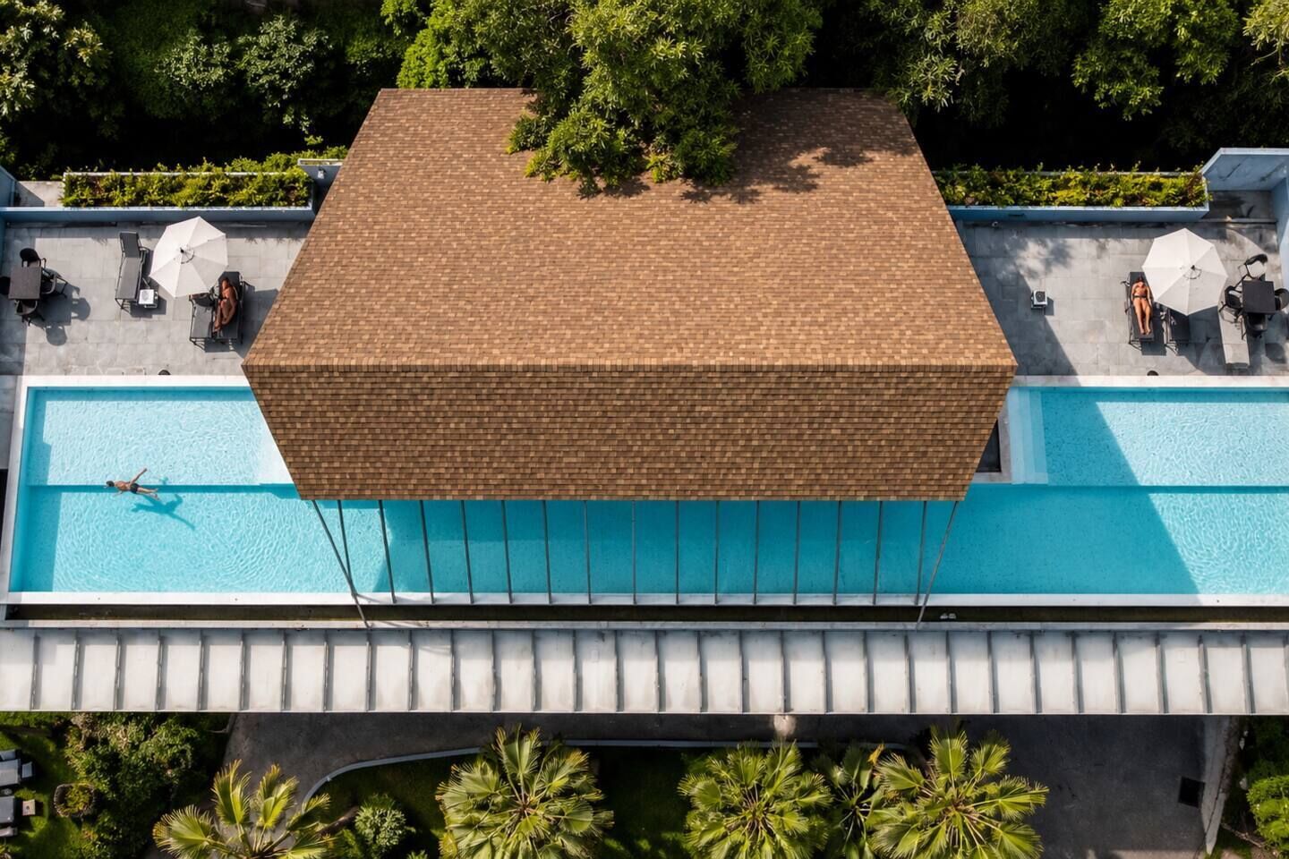 Une piscine sur le toit, recouverte d’un toit en briques, entourée de verdure et dotée de chaises longues et de parasols.
