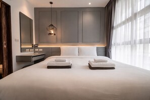 A modern hotel room with a large bed, bedside tables, a mirror, and a hanging light fixture.