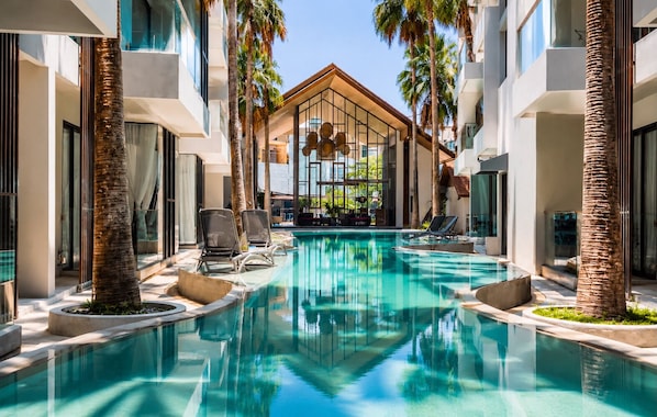 A pool area with lounge chairs, palm trees, and a building with large windows.