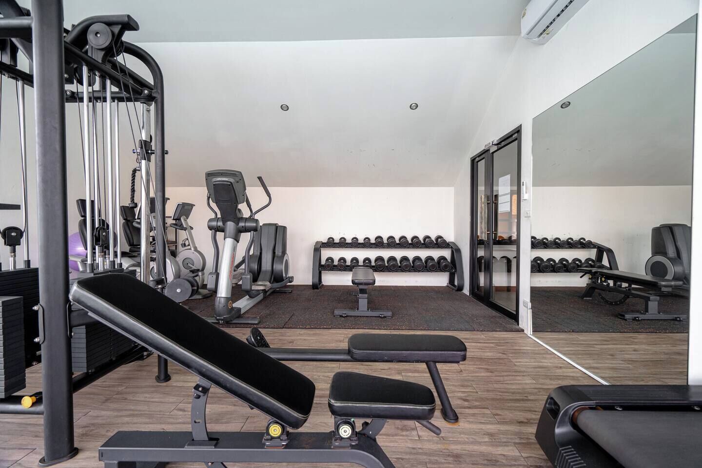 Ein Fitnessstudio mit Trainingsgeräten, Bänken und einer Spiegelwand.