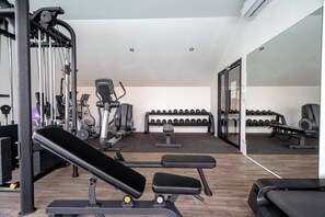 A gym with exercise equipment, benches, and a mirrored wall.