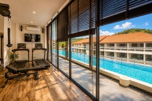 Une salle de sport équipée de tapis de course et offrant une vue sur la piscine d’un complexe hôtelier.