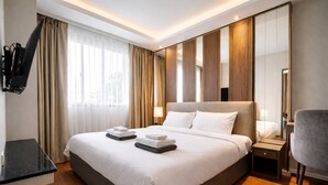 Quarto de hotel com uma cama grande, televisão de tela plana na parede, escrivaninha com cadeira e espelho.