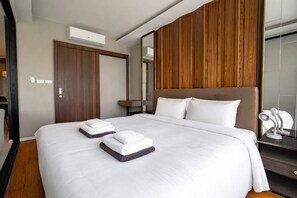 Une chambre d’hôtel avec un grand lit, deux serviettes, une tête de lit en bois, une table de chevet avec une lampe et un miroir.