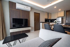 A modern living room with a flat-screen TV, a sofa, a coffee table, and a dining area with chairs and a table.