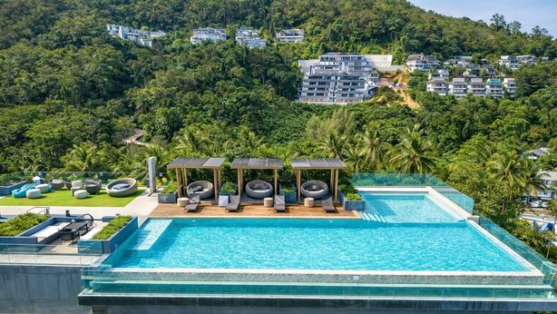 Piscina no terraço com espreguiçadeiras e pérgula, cercada por vegetação exuberante e edifícios residenciais.