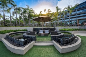 Zwembadgedeelte van een resort met een fontein, terrasmeubels en palmbomen.