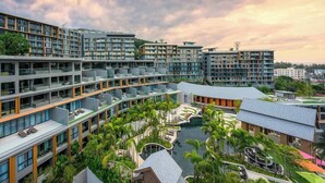Um complexo hoteleiro moderno com vários andares, piscinas ao ar livre e vegetação exuberante.