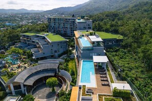 A modern hotel complex with multiple buildings, a swimming pool, and lush greenery.