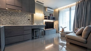 Uma sala de estar moderna com sofá, televisão e área de cozinha com painel de azulejos.
