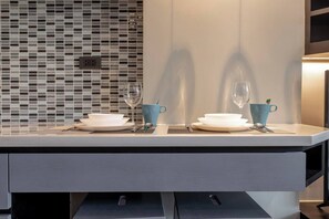 Una cocina moderna con salpicadero de azulejos, dos platos blancos, dos tazas azules y una campana extractora de acero inoxidable.