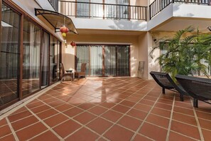 A spacious balcony with a tiled floor, a seating area with chairs, and a potted plant.