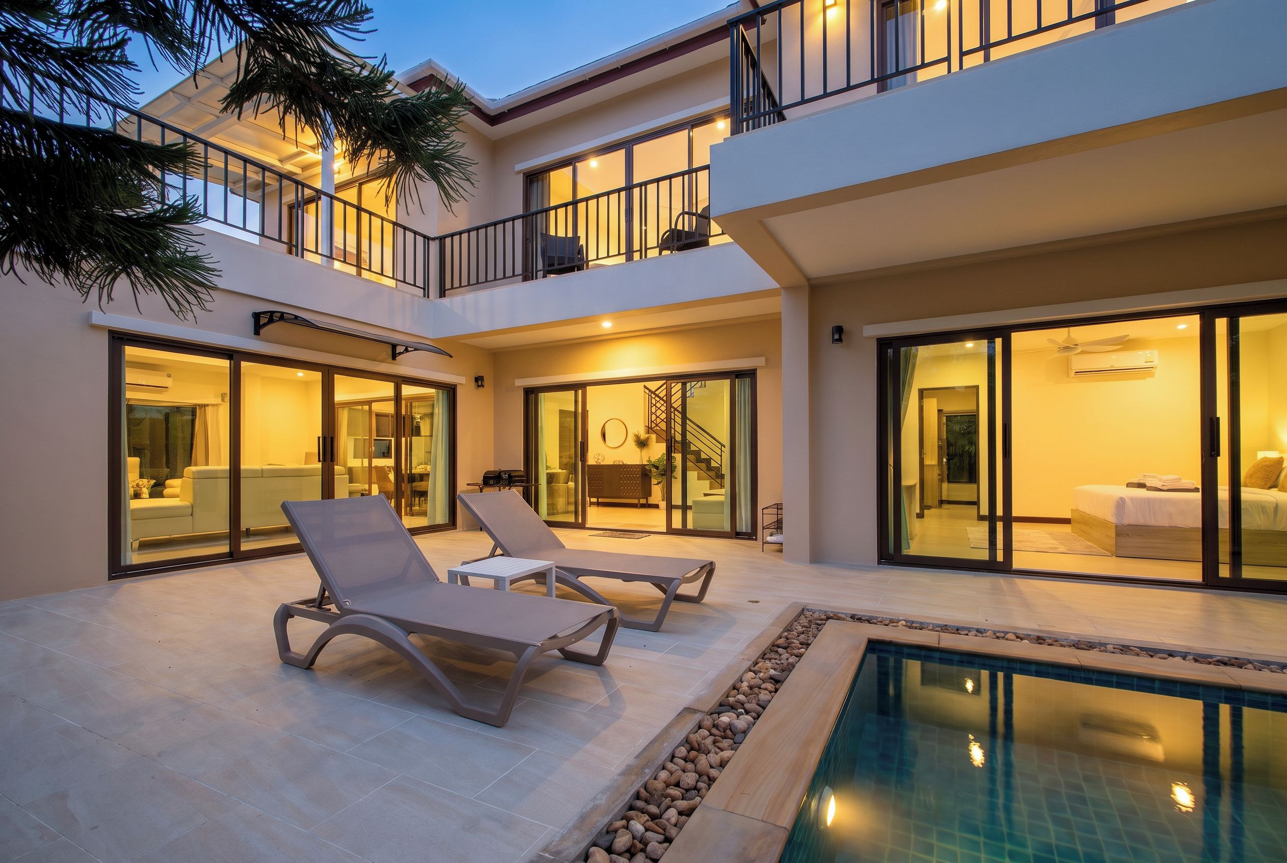 A modern two-story house with a pool, lounge chairs, and a staircase leading to the upper floor.
