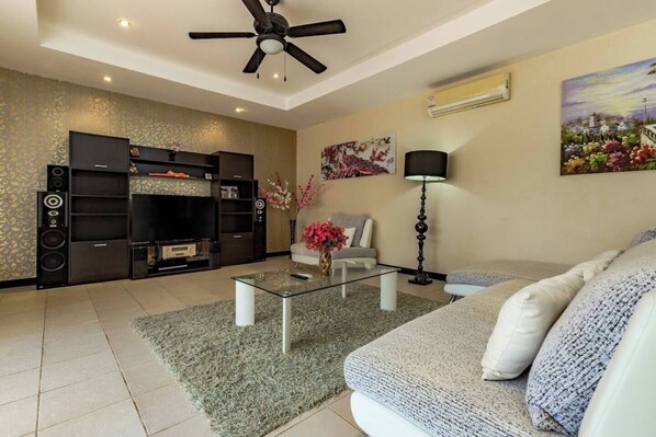A living room with a flat-screen TV, dark wooden entertainment unit, a sofa, a coffee table, and a floor lamp.