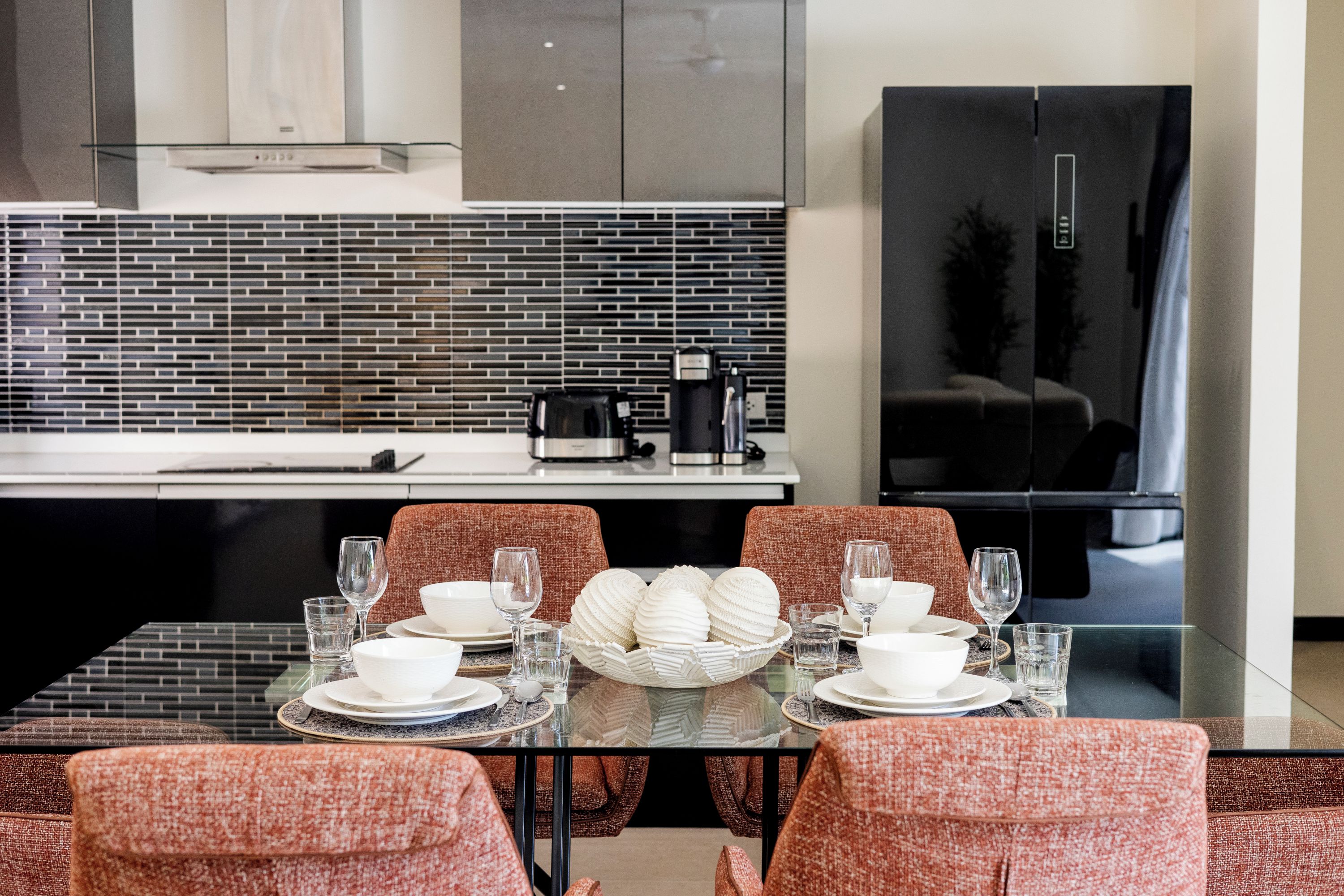 A modern dining area with a glass table set for four, surrounded by patterned chairs.