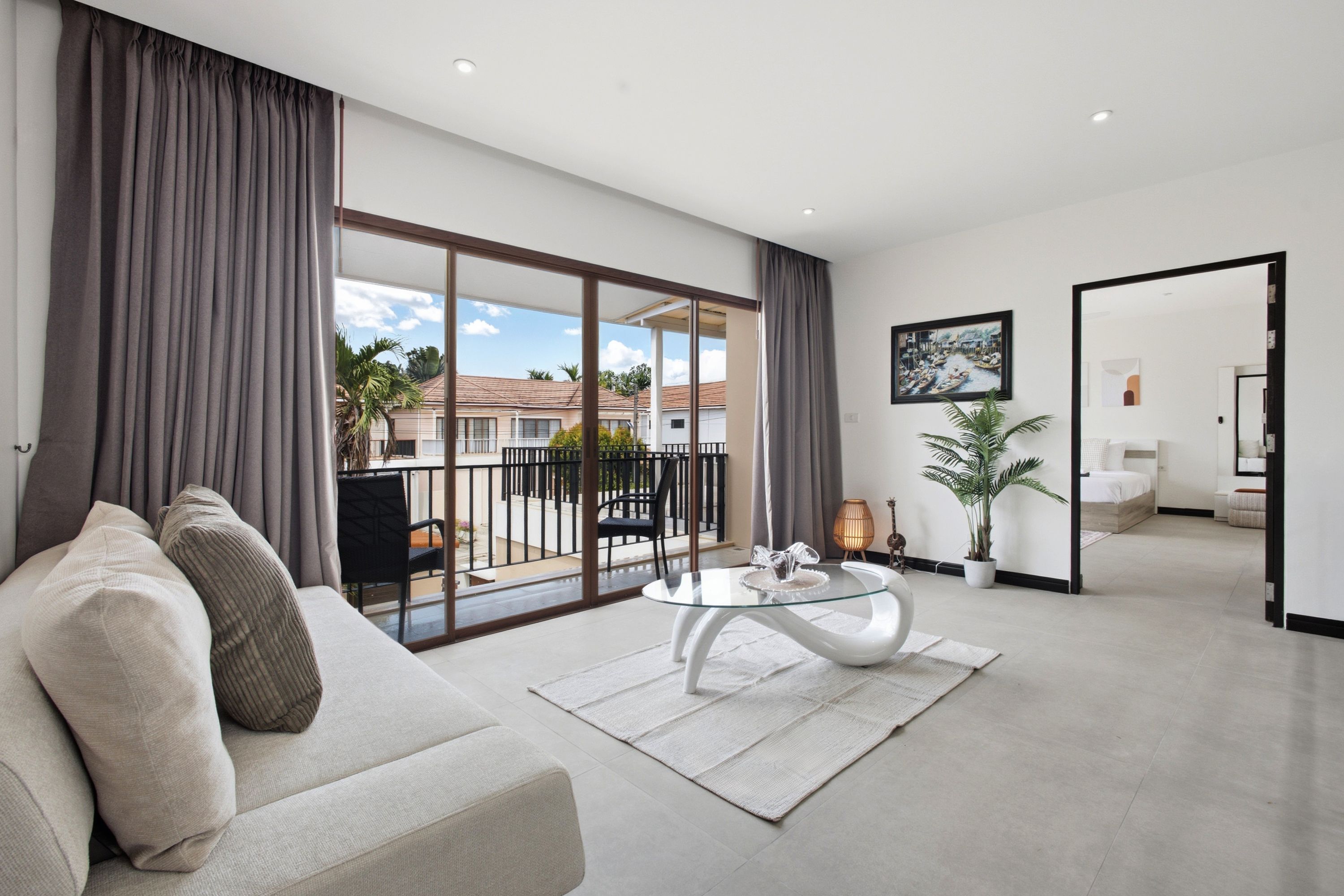 Un salon moderne avec un canapé, une table basse en verre et une vue sur un balcon aménagé avec du mobilier d’extérieur.