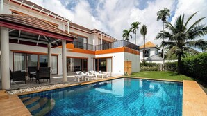 Una casa moderna de dos pisos con piscina, mobiliario exterior y palmeras.