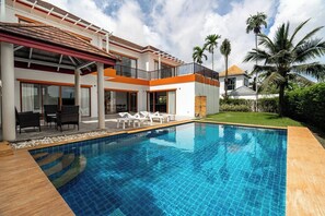 A modern two-story house with a swimming pool, outdoor furniture, and palm trees.