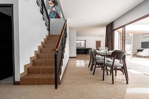 Un interior moderno con una escalera, zona de comedor y ventanas amplias.