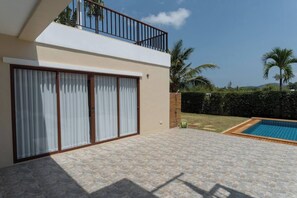 Una casa moderna de dos pisos con balcón, piscina y jardín con palmeras.