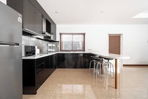 A modern kitchen with a stainless steel refrigerator, a microwave, and a coffee maker. There are bar stools at the island counter.