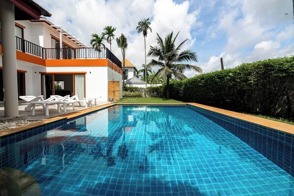 A swimming pool with a tiled edge, surrounded by lounge chairs and a building with a balcony.