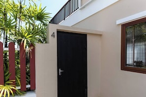 Un edificio color beige con una puerta negra, una cerca de piquetes rojos y una ventana con persianas.