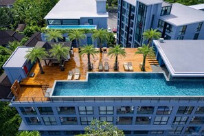 A modern hotel with a rooftop pool, palm trees, and a view of the surrounding neighborhood.